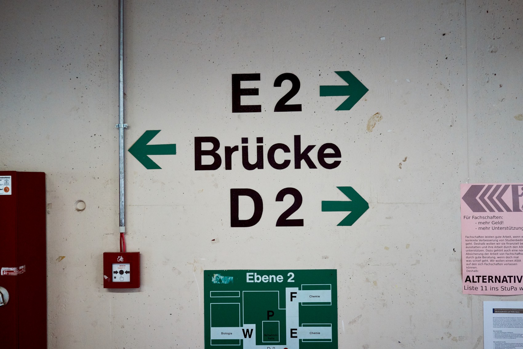 Wegweiser auf einer Betonwand. Die Pfeile weisen zur Brücke sowie zu den Ebenen E2 und D2.